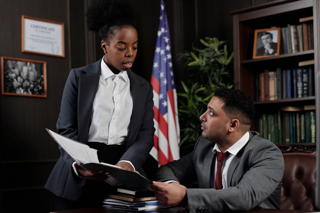 Two professionals discussing documents in an office with an American flag in the background.